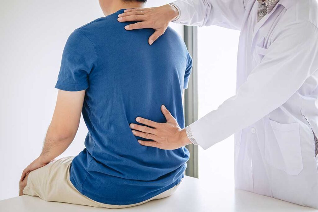 Person using a heating pad while performing a gentle lower-back stretch at home.